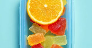 Ai提示词_一个装满五彩糖果的浅蓝色矩形容器，上面放着半片橙子，背景为浅绿色_chatgpt中文网缩略图