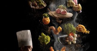 Ai提示词_一台笔记本电脑在餐饮桌上，厨师和从屏幕中漂浮出的美食，空气中弥漫着蒸汽和香料，优雅的晚宴背景，超现实主义风格，高对比度光线缩略图